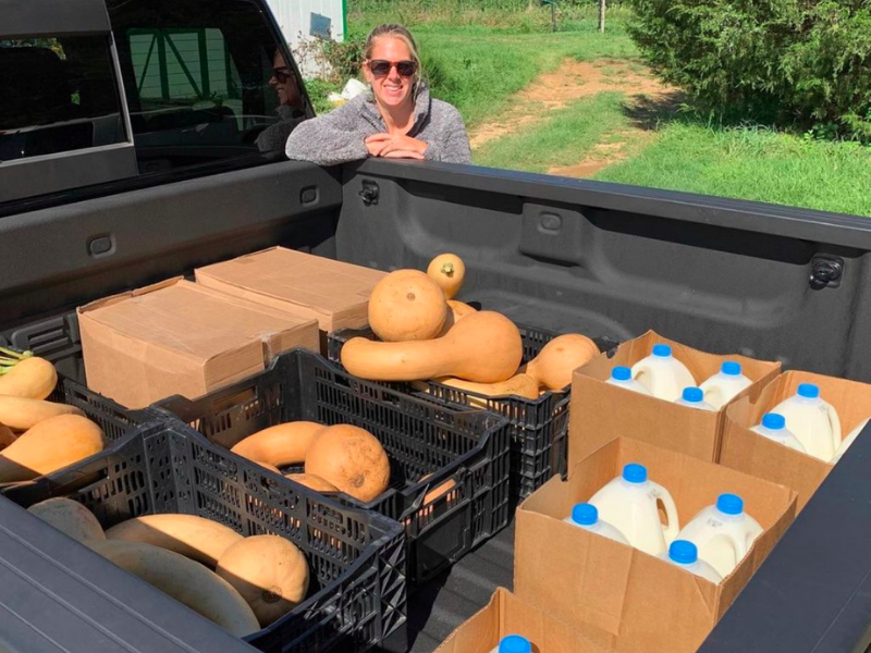 Woman standing outside pickup truck with squash and milk for food relief distribution